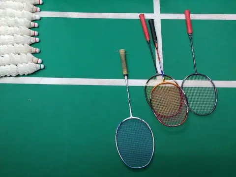 Badminton rackets and shuttlecocks on a green synthetic court