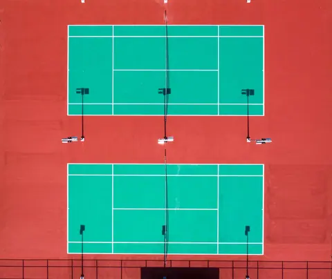 Two tennis courts seen from above with red surround and green playing area